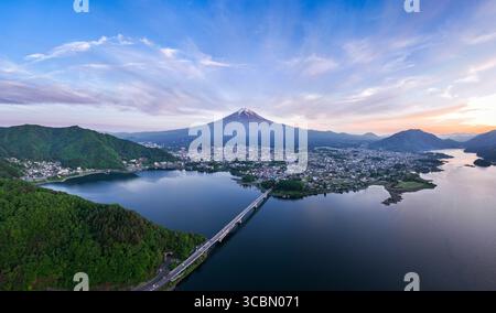 Vue aérienne du sommet enneigé du mont Fuji sur le paysage urbain reflété dans le lac tranquille, un pont reliant les rives luxuriantes, Fujikawaguchiko, Yamanashi, Japon. Banque D'Images