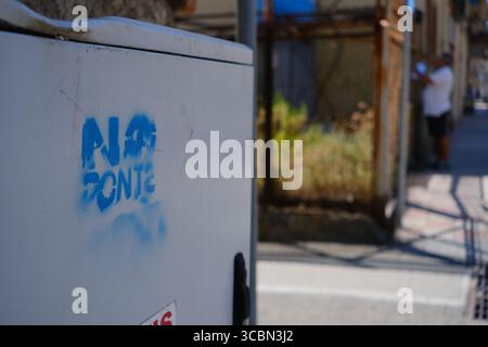 Messine, Sicile, Italie – août 2025. Le vice-premier ministre et ministre de l’infrastructure, Matteo Salvini, assiste à un déjeuner au restaurant Grecale pour célébrer l’approbation par le CIPESS du projet controversé du pont du détroit de Messine. Sur la plage voisine, les baigneurs partagent le sable avec les manifestants tenant un drapeau « No Ponte » (No Bridge) contre la construction. Dans l'eau, un bateau de pêche traditionnel de Messine appelé felouca, utilisé pour la chasse à l'espadon, est décoré de drapeaux italiens de la Lega Nord de droite. Villa San Giovanni en Calabre est visible en arrière-plan. Banque D'Images