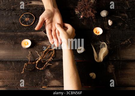 Mains féminines entourées de coquillages et de bougies, de racines, de mèches de cheveux et d'objets magiques sur une surface en bois comme un rituel de sorcière Banque D'Images