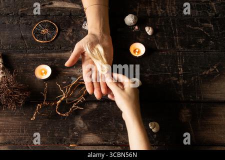 Mains féminines entourées de coquillages et de bougies, de racines, de mèches de cheveux et d'objets magiques sur une surface en bois comme un rituel de sorcière Banque D'Images