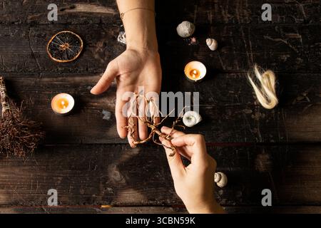 Mains féminines entourées de coquillages et de bougies, de racines, de mèches de cheveux et d'objets magiques sur une surface en bois comme un rituel de sorcière Banque D'Images