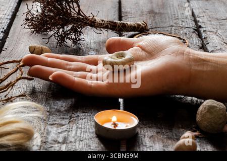 Main féminine avec coquille entourée de bougies, racines, mèches de cheveux et objets magiques sur la surface en bois comme un rituel de sorcière Banque D'Images