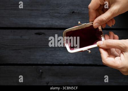 Mains féminines tenant un portefeuille vide ouvert sur une surface en bois sombre, vue de dessus Banque D'Images