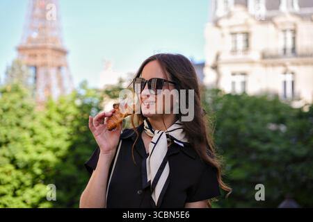 Femme mangeant un croissant près de la Tour Eiffel à Paris Banque D'Images