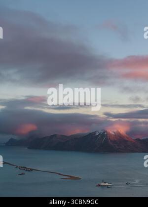 Vue aérienne des montagnes recouvertes de rougeur de neige sous le ciel pastel alors que l'océan rencontre la terre près d'Unalaska, Alaska, États-Unis. Banque D'Images