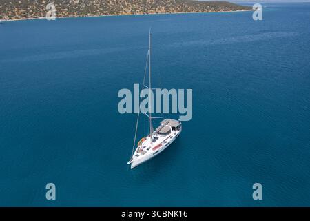 Vue aérienne d'un voilier solitaire glisse à travers l'étendue turquoise, une danse sereine de blanc contre le bleu profond, Spetses, Nisi, Grèce. Banque D'Images