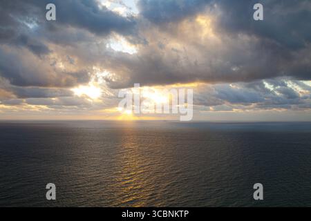 Vue aérienne de la lueur rayonnante du soleil perçant à travers des nuages spectaculaires et se reflétant sur la surface tranquille de l'océan Atlantique, Miami Beach, Floride, ONU Banque D'Images