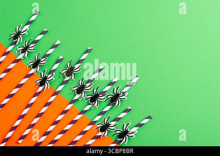 Pailles en papier avec des décorations d'araignée noire sur fond vert et orange pour la fête d'Halloween et la célébration écologique. Vue de dessus, pose à plat, copie s Banque D'Images