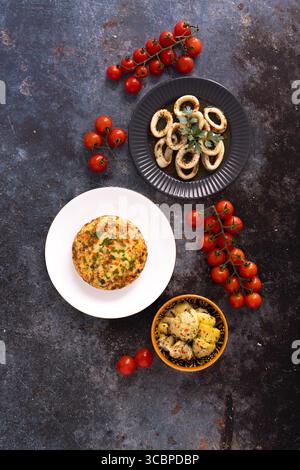 Plat de la sélection de mezzés M&S avec anneaux de calamars frits, frittata de légumes, artichauts marinés et tomates cerises sur un fond rustique. Banque D'Images