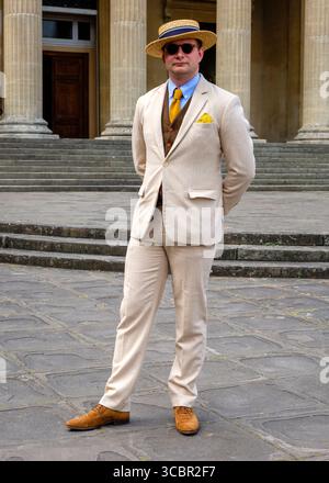 Un homme en costume de couleur claire, chapeau de paille et lunettes de soleil se tient devant un bâtiment avec des colonnes et des marches. Banque D'Images