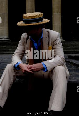 Un homme en chapeau de paille et costume est assis sur des marches devant de grandes colonnes. Banque D'Images