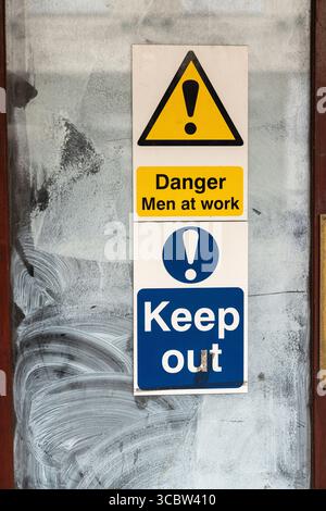Danger les hommes au travail et garder à l'extérieur panneaux d'avertissement de sécurité sur une porte vitrée à Warminster, Wiltshire, Angleterre Royaume-Uni Banque D'Images