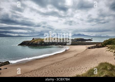 Porth TWR Bach et le vieux phare sur l'île de Llanddwyn montrant l'affleurement cambrien de MELANGE avec la péninsule de Llyn en arrière-plan Banque D'Images