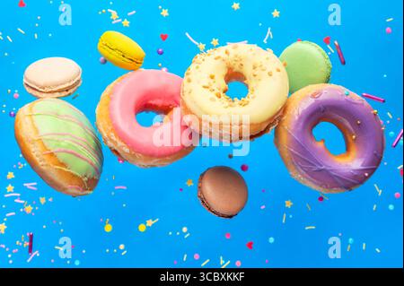 Nourriture en lévitation. Beignets colorés savoureux avec macarons et arroseurs volant sur fond bleu. Concept de célébration. Banque D'Images