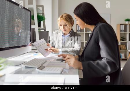 Deux femmes comptables financières examinant des documents financiers et analysant des feuilles de calcul au bureau. Banque D'Images
