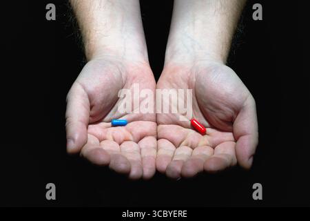 Choisissez votre concept de destin. Mains masculines tenant des capsules de pilules rouges et bleues sur fond noir. Banque D'Images