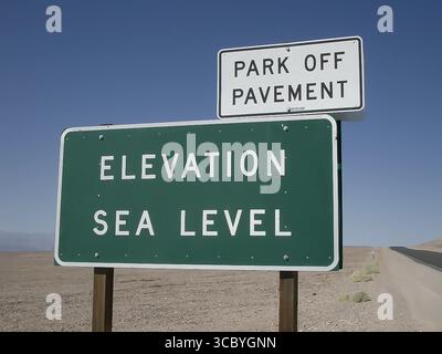 Panneau dans un paysage désertique indiquant « ÉLÉVATION DU NIVEAU DE LA MER » et un avertissement séparé indiquant « STATIONNER HORS DU TROTTOIR ». Banque D'Images