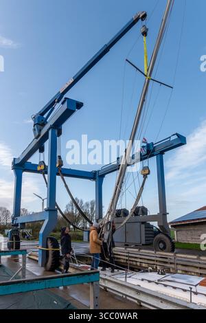 Warns, pays-Bas - 20 novembre 2023 : grue de levage de bateau hissant un voilier hors de l'eau dans une marina animée, avec des travailleurs manipulant habilement Banque D'Images