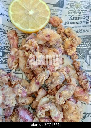 Une portion de dentelle frite servie sur une assiette blanche avec du journal imitation comme décoration, il y a une tranche de citron sur l'assiette. Banque D'Images