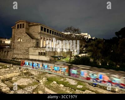 Ruines de basilique romaine avec passage de métro couvert de graffitis, Agora antique et Acropole en arrière-plan, Athènes, Grèce la nuit. Banque D'Images