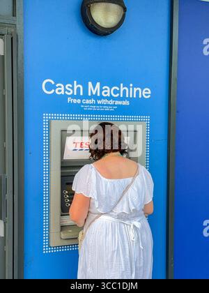 Pontypridd, pays de Galles, Royaume-Uni - 12 juillet 2025 : personne retirant de l'argent d'un distributeur de billets à l'extérieur de la succursale de Tesco Express dans le centre-ville de Pontypridd Banque D'Images