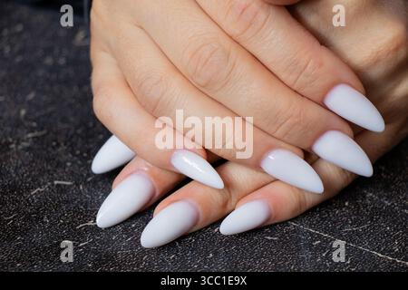 Mains féminines avec une longue manucure blanche pointue sur fond noir gros plan Banque D'Images