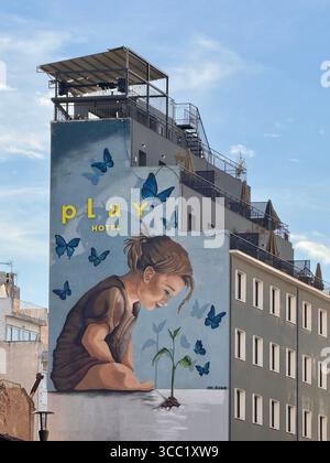Peinture murale d'art de rue sur un bâtiment à Athènes représentant un enfant interagissant avec la nature, entouré de papillons et du mot « jeu ». Banque D'Images