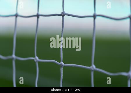 Le détail du filet de but de football montre la texture du filet noué blanc contre un terrain de jeu vert flou Banque D'Images