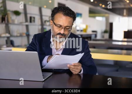 Sérieux homme dirigeant indien aîné et concentré lisant le document attentivement Banque D'Images
