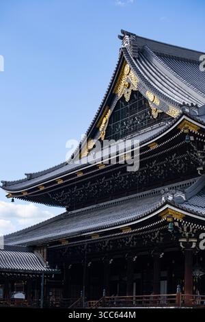 Vue rapprochée du temple Higashi Hongan-ji présentant des éléments architecturaux complexes et un design élégant du toit sous un ciel bleu clair. Capture des Banque D'Images
