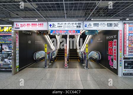 Vue de face d'une entrée d'escalator à Yodobashi Camera Multimedia Kyoto, entourée de publicités colorées et de panneaux. La scène capture le live Banque D'Images
