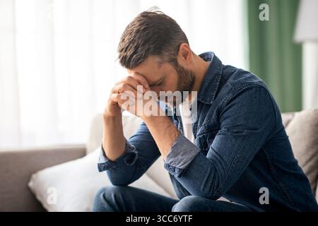 Homme déprimé assis sur un canapé dans la salle de séjour Banque D'Images