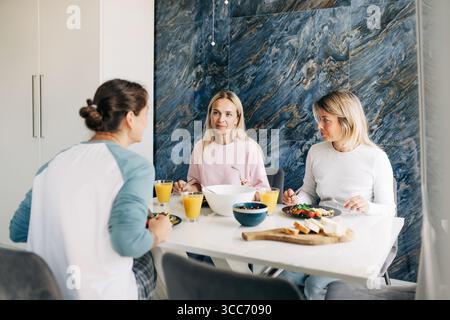 Trois femmes amies déjeunent ensemble assis à une grande table dans un appartement confortable. Banque D'Images