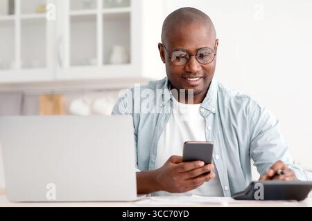 Concept d'épargne et de finances. Homme noir mature utilisant une calculatrice, un téléphone et un ordinateur portable Banque D'Images