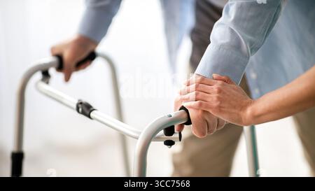 Homme âgé méconnaissable utilisant un marcheur, jeune médecin le soutenant et l'aidant à la maison de retraite Banque D'Images