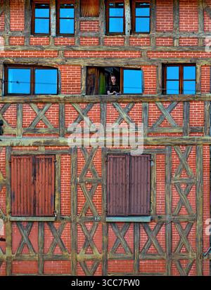 Femme regarde une maison à plusieurs étages avec une façade en briques rouges et bois brun à Figeac dans la région du Périgord, France; Banque D'Images