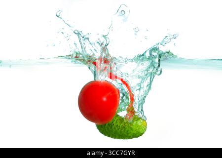 Éclaboussure vibrante créée par une tomate rouge entrant en collision avec un concombre vert, entourée de gouttelettes d'eau claire. Banque D'Images
