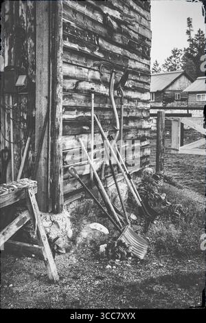 Image en noir et blanc d'un mur de grange en bois altéré avec des pelles, des râteaux et d'autres outils de ranch appuyés contre elle, situé dans un ranch du Wyoming avec l Banque D'Images