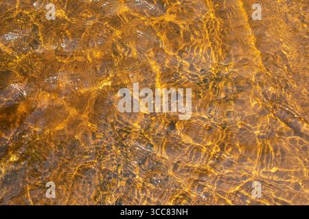 Eau de rivière peu profonde avec des ondulations et des reflets du soleil à sa surface. Texture de fond abstraite Banque D'Images