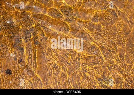 Eau de rivière peu profonde avec des ondulations et des reflets du soleil à sa surface Banque D'Images