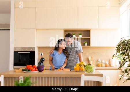 Un couple profite d'un moment agréable pour préparer un repas dans une cuisine élégante. Ils hachent des légumes, partagent des sourires et créent une atmosphère chaleureuse Banque D'Images