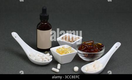 Vitamines assorties et capsules avec teinture dans un flacon compte-gouttes sur fond gris, concept holistique de santé et de nutrition. Banque D'Images