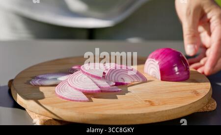 le chef coupe l'oignon rouge frais sur une planche à découper pour préparer un repas sain. cuisine extérieure, gros plan sur la nourriture Banque D'Images