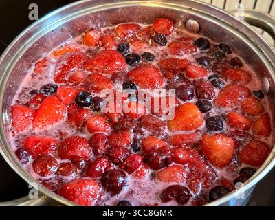 Diverses baies rouges bouillent dans une casserole. Processus de confiture maison, gros plan de la nourriture Banque D'Images
