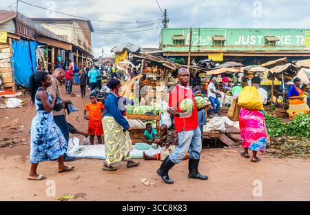 Un Africain de la région transporte une paire de gros melons sur un marché alimentaire animé en bord de route dans un village près de Kampala, région centrale, Ouganda Banque D'Images