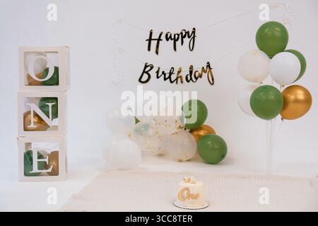 Une configuration de premier anniversaire magnifiquement décorée comprend de grands blocs D'UNE lettre, des ballons dorés et verts, et un gâteau mignon, créant un joyeux et festi Banque D'Images