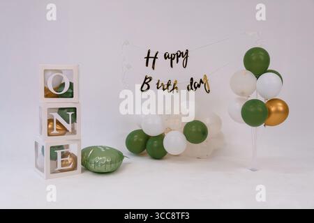 Un cadre de fête d'anniversaire dynamique avec de grands blocs, des ballons verts, blancs et or, créant une atmosphère festive pour la célébrité d'un bébé Banque D'Images