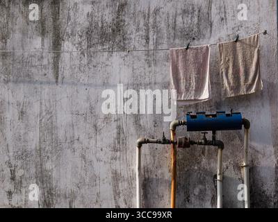 Deux petites serviettes assaisonnées sur une corde à linge avec pince à linge et contre un grunge rustique taché murs blancs avec compteur d'eau et tuyaux. Banque D'Images