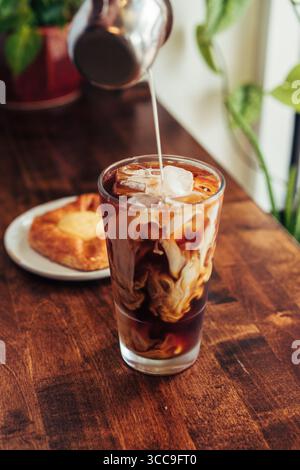 Crème tourbillonnant dans du café glacé avec de la pâtisserie Banque D'Images