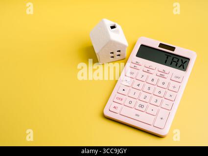 Impôt foncier, taux d'intérêt immobilier, concept de planification financière de la maison. "TAXE" sur l'affichage de la calculatrice rose et modèle miniature de maison blanche sur Yell Banque D'Images